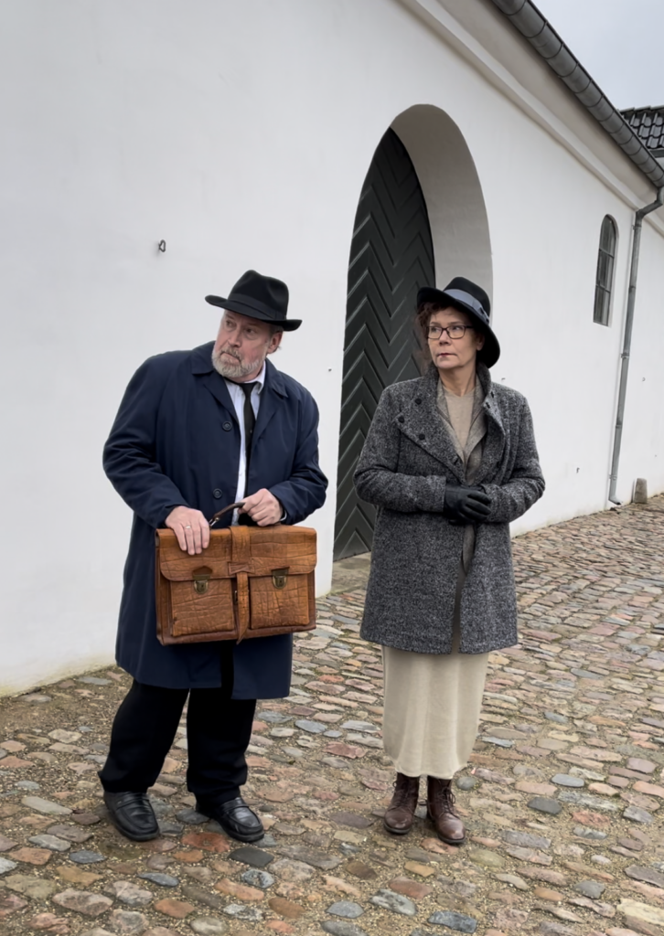 Med Gestapo i hælene. To skuespillere i rollen som modstandsfolkene Erik og Gerda står i kostumer fra 1940 foran Staldgården og skuer nervøst til siden